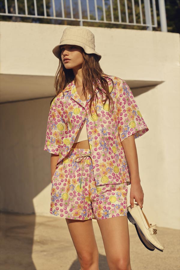 Bộ trang phục gồm áo sơ mi ngắn tay và quần shorts trên nền họa tiết đặc trưng của BST Smiley